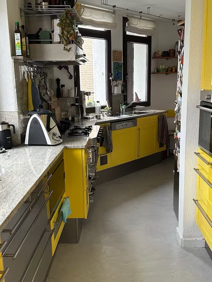 Handyfoto einer schmalen Küche mit gelben Fronten, Granitarbeitsplatte und Fenstern, flaues Licht und graue Farben